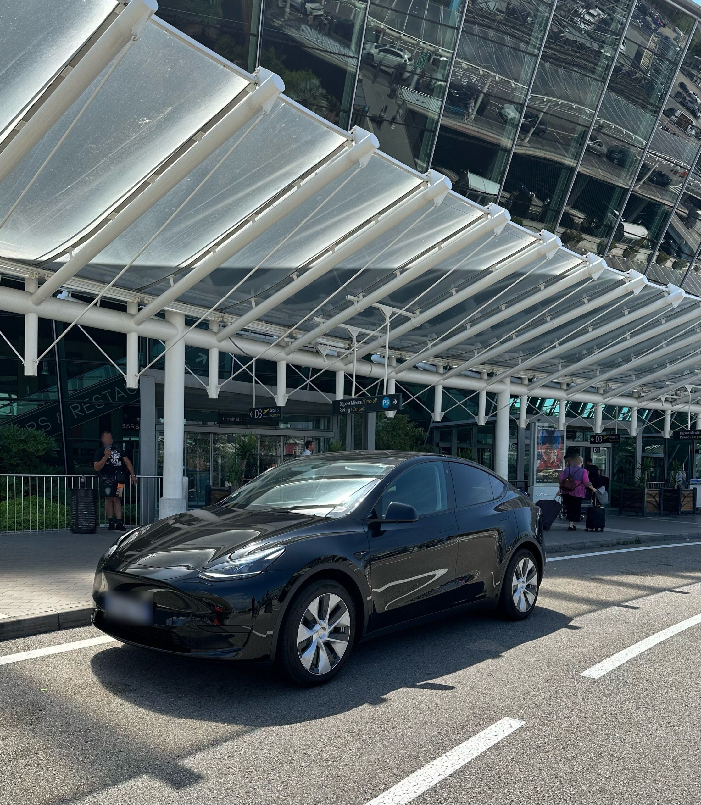 Tesla noire stationnée devant un bâtiment vitré à auvent blanc.