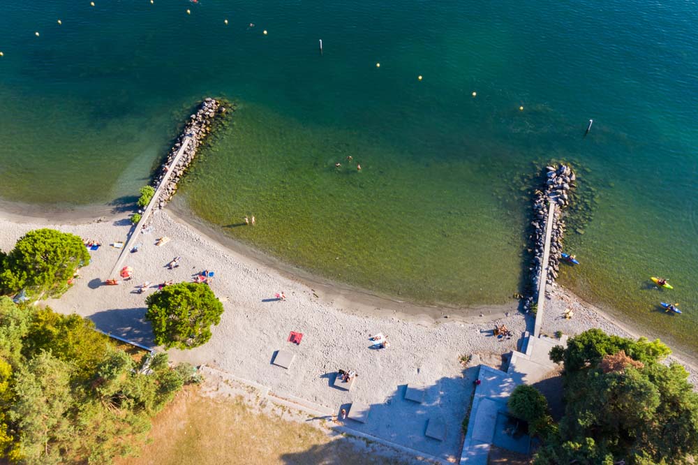 Vue aérienne d’une petite plage bordée de deux digues, avec des baigneurs dans l’eau.