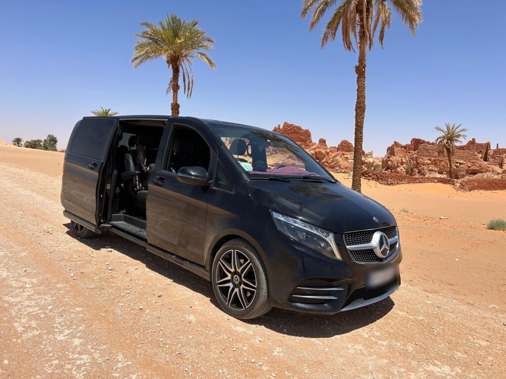 Van Mercedes noir stationné dans un paysage aride avec des palmiers, portière coulissante ouverte.